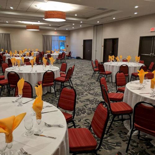 A banquet hall set up with round tables and red chairs, featuring yellow folded napkins and place settings on each table, ready for an event.