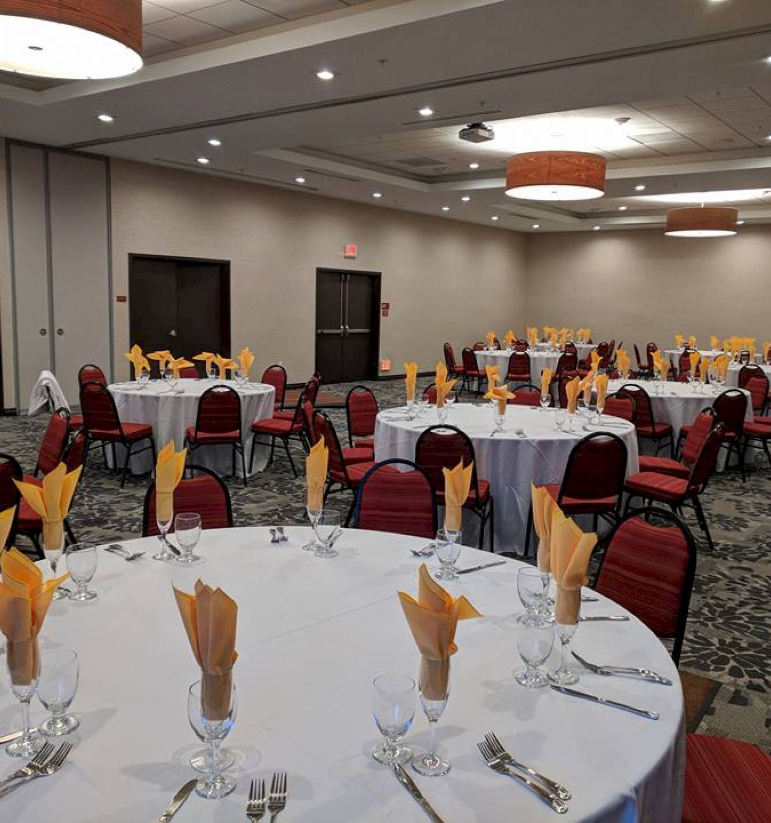 A banquet hall with round tables set for an event, featuring red chairs, yellow napkins, and silverware in a spacious, well-lit room.