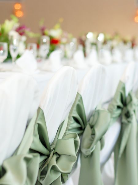 A banquet table with green bow-tied chair covers, white tablecloths, and floral centerpieces, set for an event or celebration.