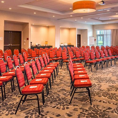 A conference room setup with red chairs arranged in rows, a podium in front, and a large screen displaying a logo and welcome message at the back.