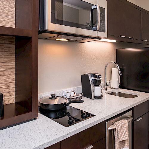 A compact kitchen with a countertop, microwave, sink, coffee maker, mini-fridge, toaster, and stove with a pan.